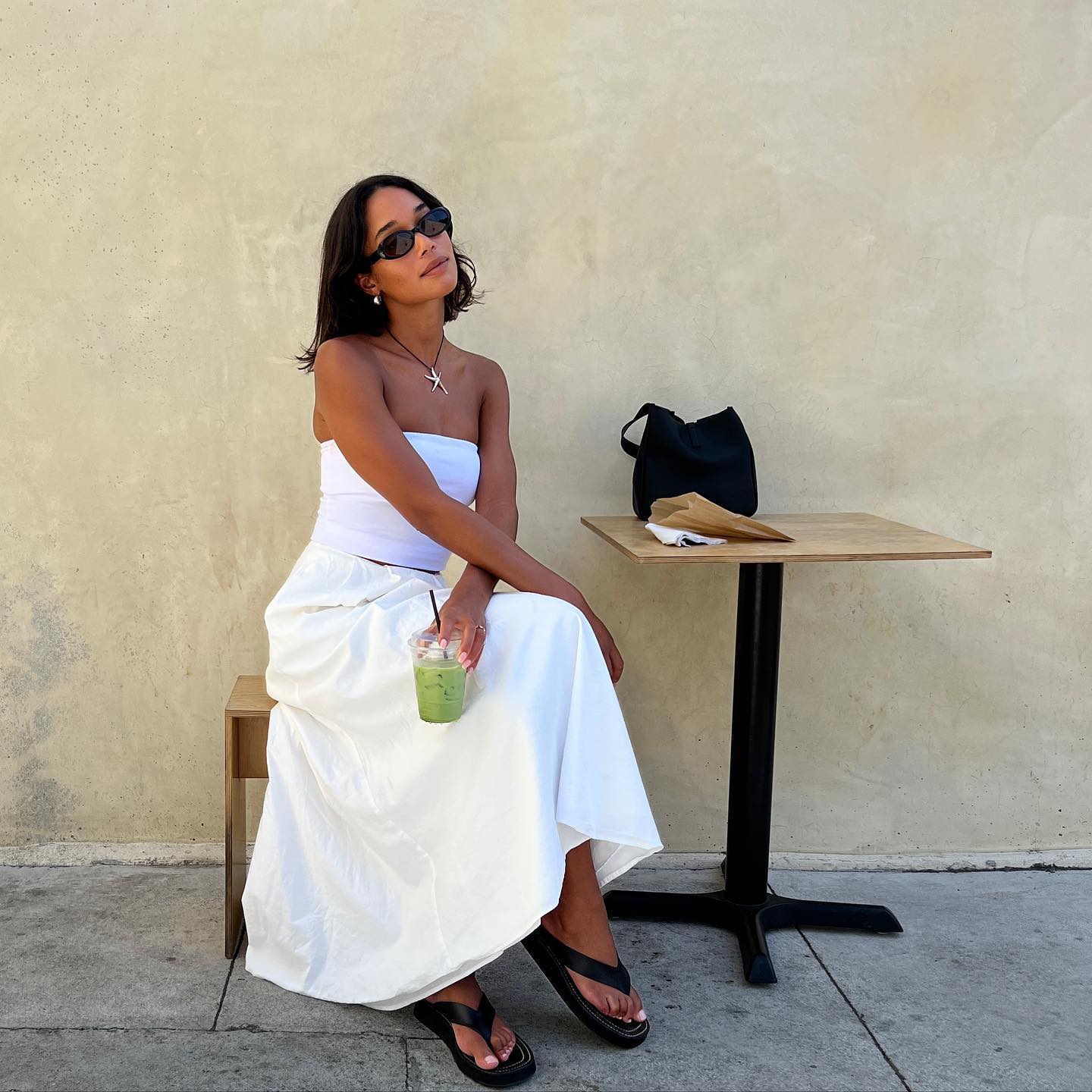 An image of Laura Harrier wearing a white linen skirt with a matching white bandeau and platform flip-flops while in Los Angeles.
