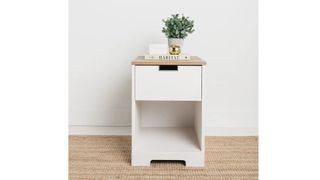 Fenley 1 Drawer Nightstand in White/Warm Brown, on top of a jute carpet, against a white wall