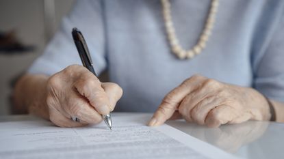 An older woman signs paperwork, only her hands showing.