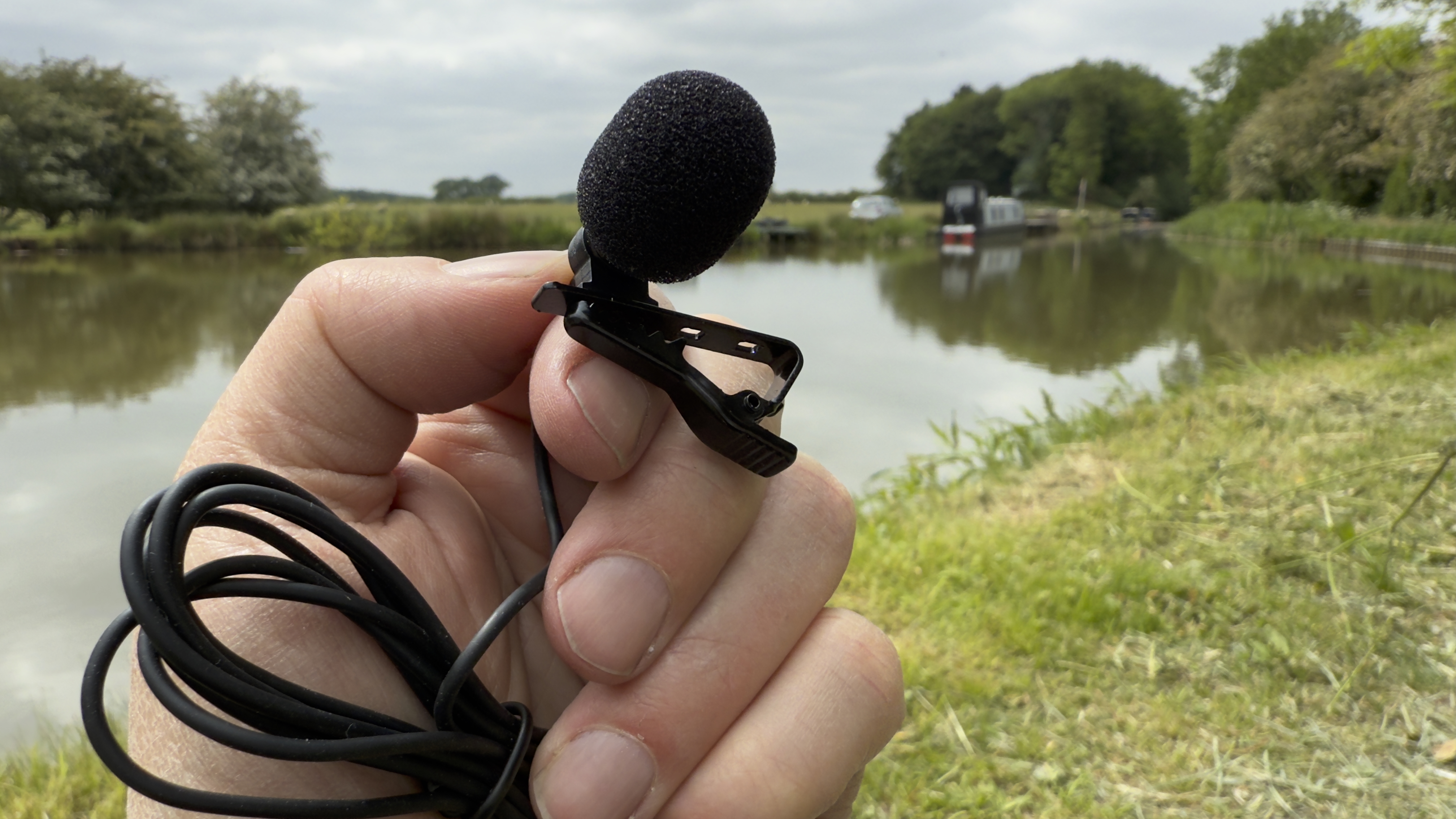 A hand holds one of the two supplied lavalier clip mics. It’s wearing a little foam windshield