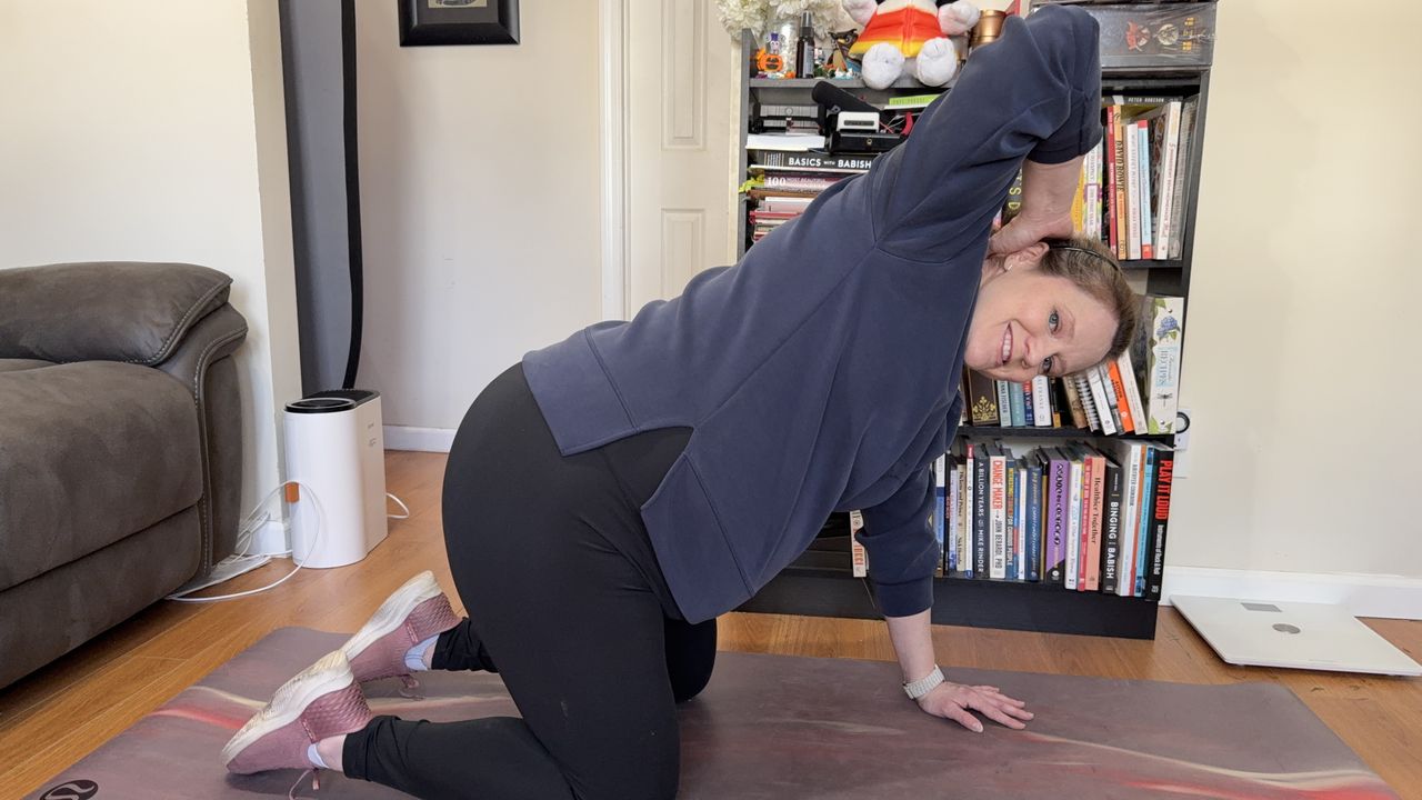Jennifer Rizzuto performs a thoracic stretch. She is balancing on her knees and her left hand while her right hand is behind her head. Her elbow is pointing up to the ceiling.