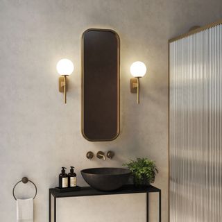 Wall lights on wall of bathroom with brass mirror hung between them