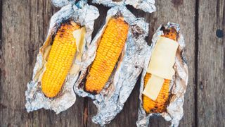 Three corn on the cobs grilled in foil with butter and cheese