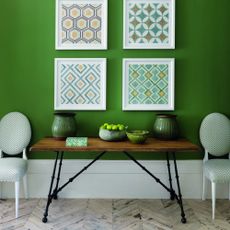 A green-painted hallway with framed artworks, a console table and two chairs