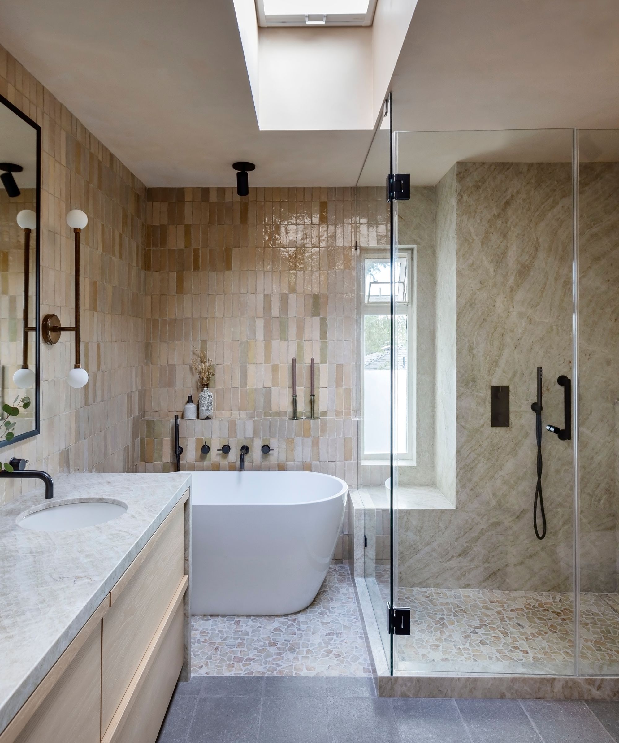 Neutral bathroom with texture tiles and wooden vanity, a white bath tub and gold and black accents
