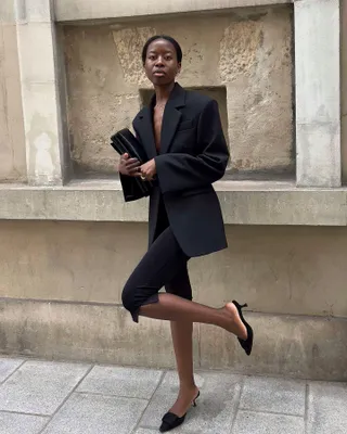 Woman in black blazer, capri pants, and mules.