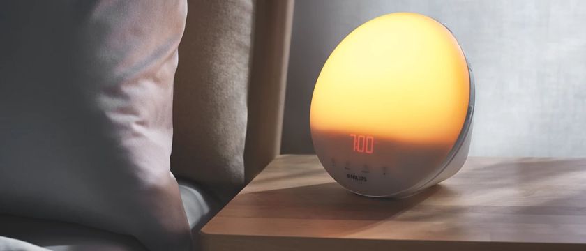 The image shows the Philips SmartSleep Sleep and Wake-Up on a bedside table in a dimly lit room