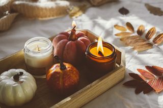 A wooden tray decorated with autumnal candles, pumpkins, and autumn foliage.