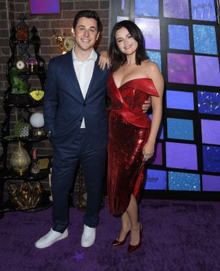 A photo of Selena Gomez wearing a red sequin strapless dress and posing next to former co-star David Henrie