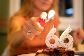 Woman lighting birthday cake with "66" candles.