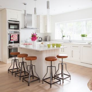 all-white kitchen with island and industrial-style bar stools, with laminate flooring