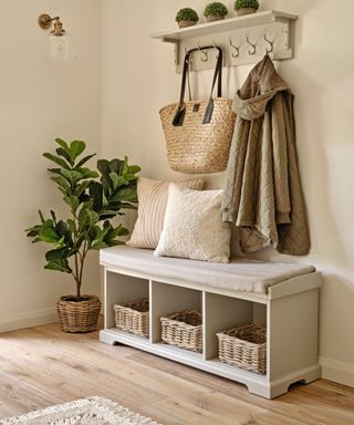 A small entryway with a white storage bench and white wall hooks with a bag and coat