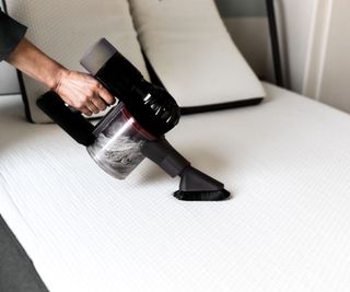 A handheld vacuum being used on a white sofa