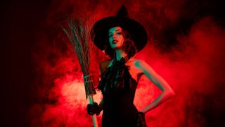 woman in a witch halloween costume in a red background
