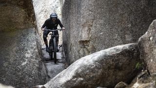 A mountain biker traversing a narrow rock garden between two rock formations