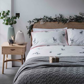 a bedroom with white walls and wood furniture, with a reindeer duvet set on the bed and faux leaf garland draped over the headboard