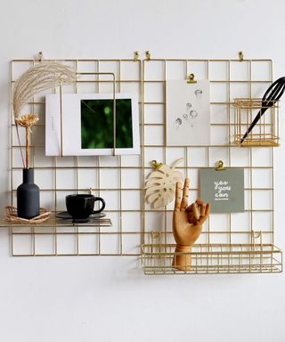 An image of a gold wire peg board on a neutral wall with shelves and baskets attached to it