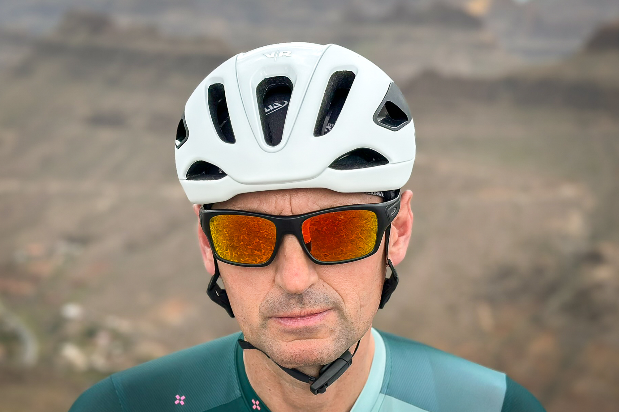 Front view of a man wearing a white helmet, sunglasses and a green jersey