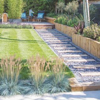 Lawn with stripes next to gravel pathway with stepping stones and ornamental grasses