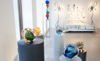 Colourful glass orbs on podiums and a bed in front of drawn wall art