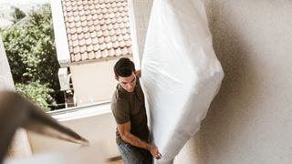 A man moves a mattress on his own up a flight of stairs