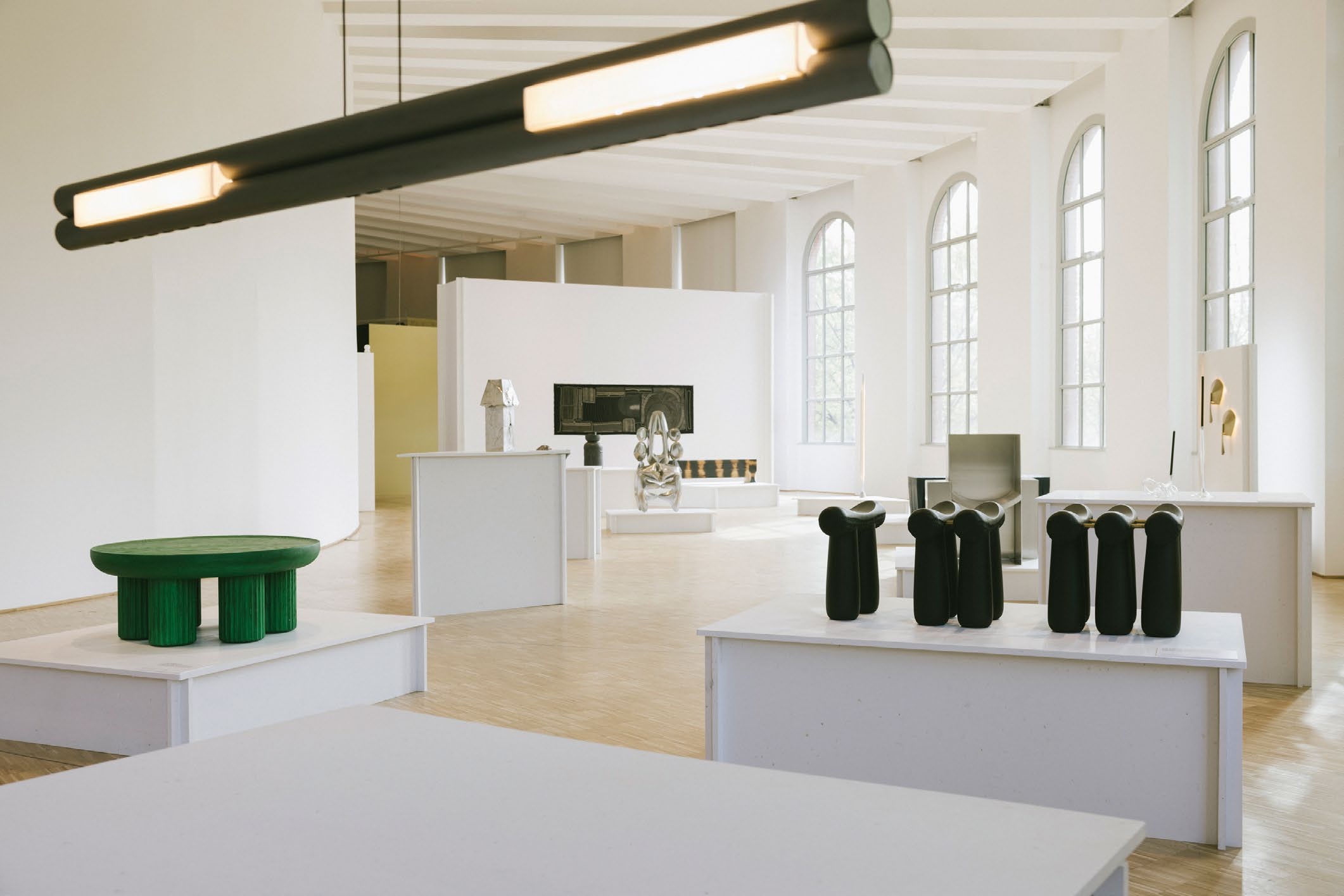 A spacious art gallery featuring modern sculptures and minimalist furniture, reflecting the innovative designs showcased during Wallpaper's exhibition during Milan Design Week.