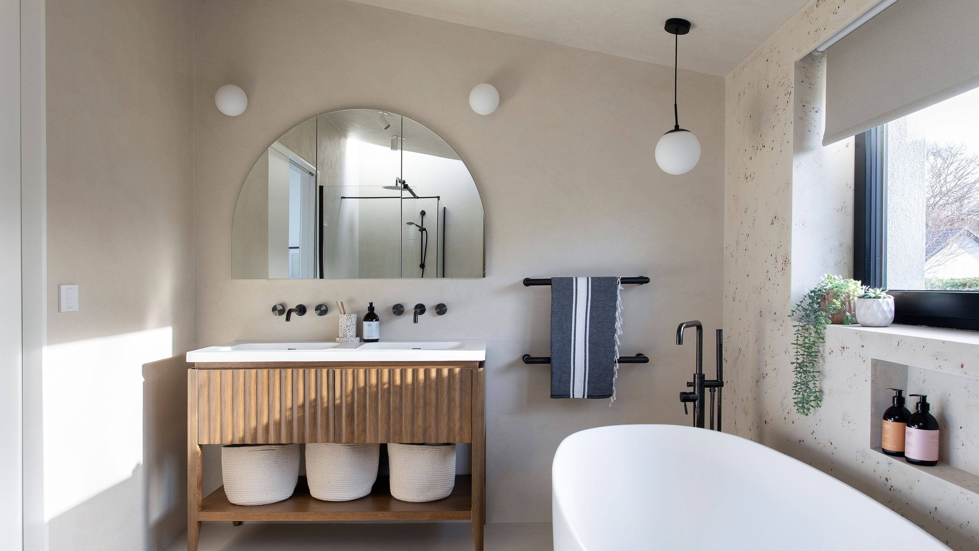 White bathroom with a bathtub, wooden vanity and arch mirror