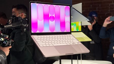 The Apple MacBook Neo in pink and yellow at an event