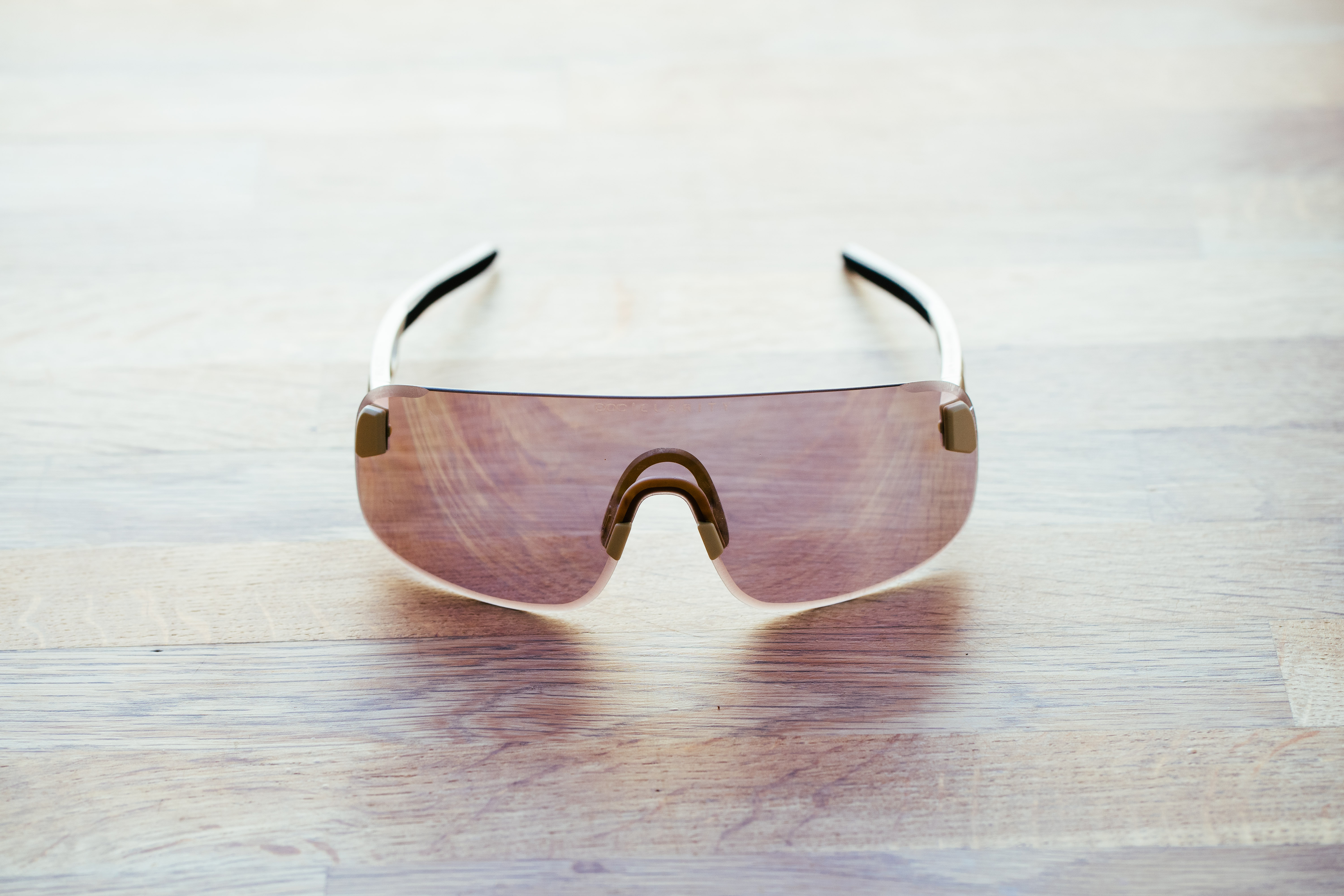 A set of frameless sunglasses with beige arms on a wooden surface
