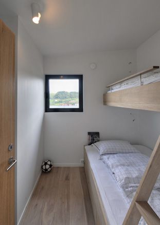 Interior view of a bedroom at Trekronekabin featuring a white ceiling with a light fixture, white walls, a small square window, wood flooring, wooden bunk beds with white and grid style pillows and linen and a football in the corner