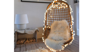 The pom pom string lights from Oliver Bonas draped around a hanging chair.