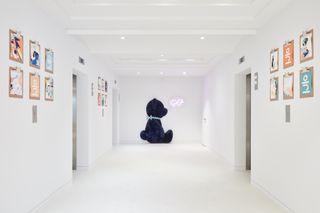 A corridor with all-white walls, floors and ceiling with colourful typographic posters on the walls and the blue silhouette of a bear on one side
