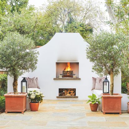 White outdoor fireplace in garden with potted trees and plants