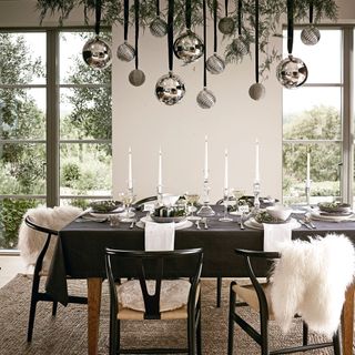 a white dining room with black table and black dining chairds with large silver baibles hanging down over the table and candles and tableware on the table