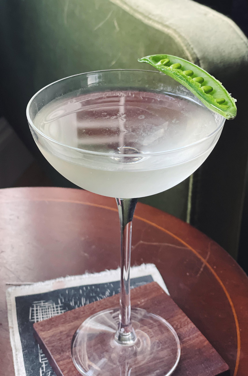 Cocktail on a table with a pea pod garnish