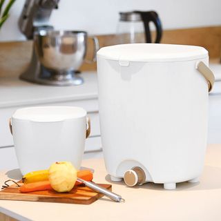 Two white plastic bin caddies said on a white worktop in a kitchen with peeled vegetables on a board next to them