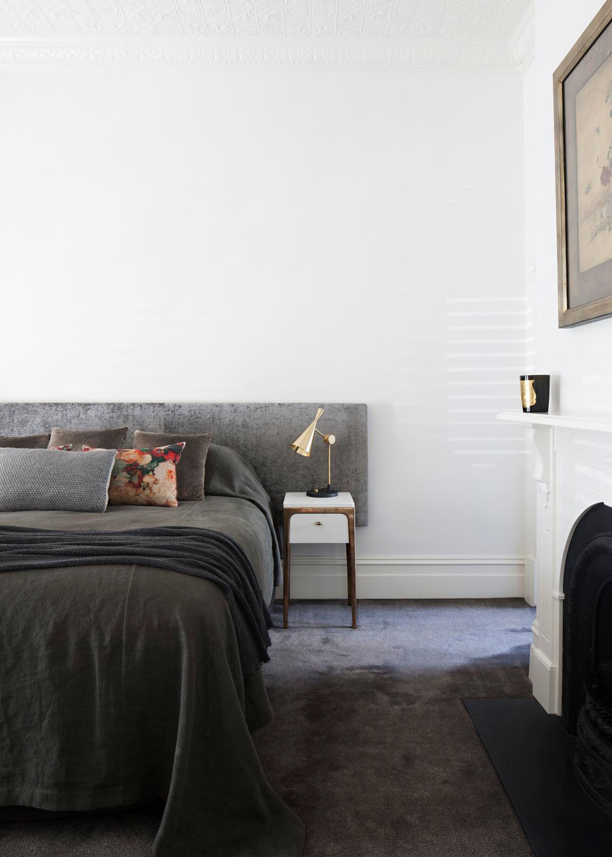 A white bedroom with a gray bed, a fireplace and framed art on the wall