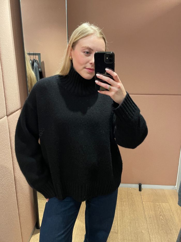 Woman wears black funnel-neck jumper and blue jeans