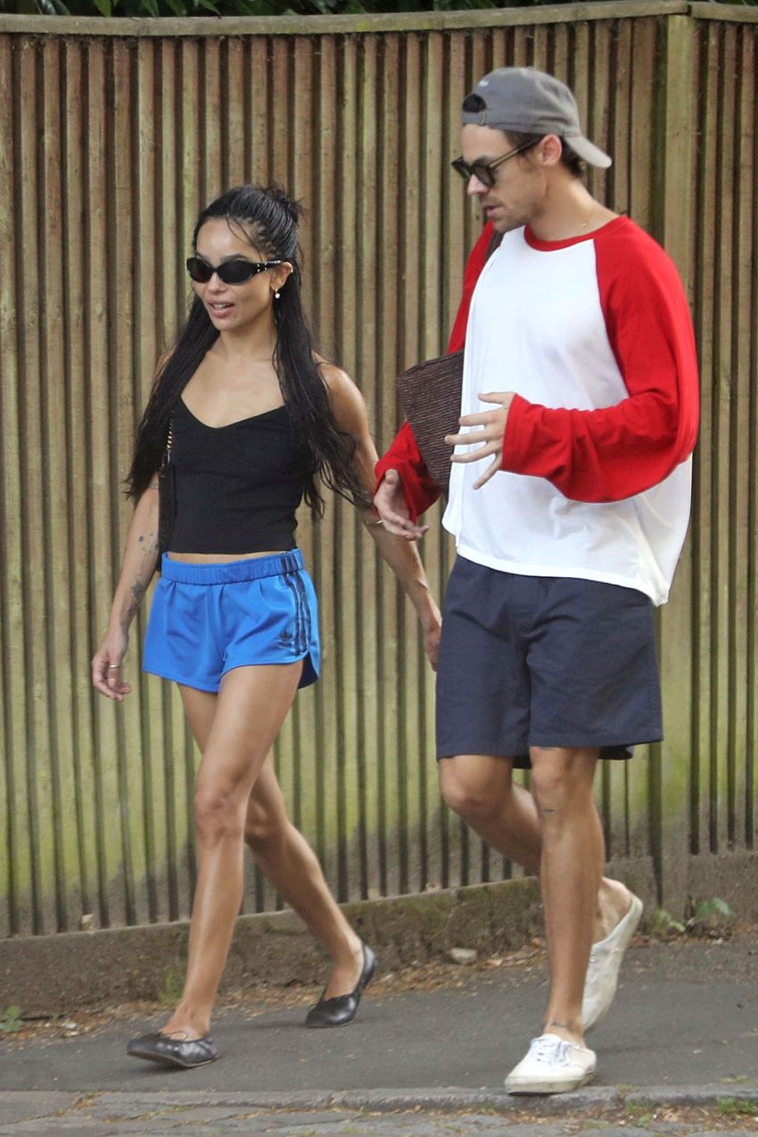 Zoe Kravitz wearing black sunglasses, a black tank top, blue shorts, and black flats.