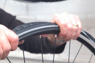 fix a puncture mend an inner tube image shows a pair of hands gripping a wheel and rolling the tyre in to place on the rim