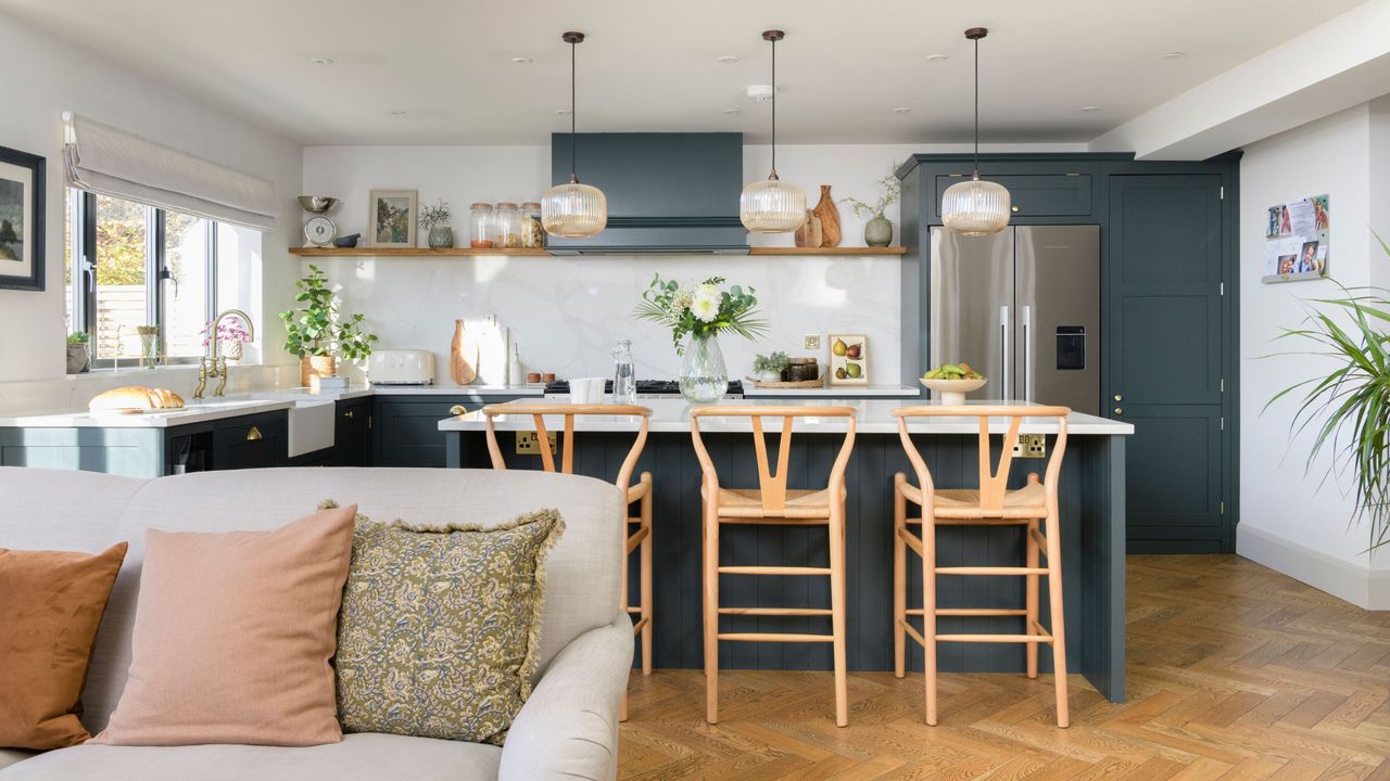 Open plan kitchen area with blue cupboards and a matching kitchen island, with high stools and a cream sofa