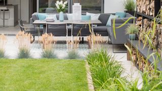 backyard with lawn area framed with planted grasses with dining table on a patio terrace