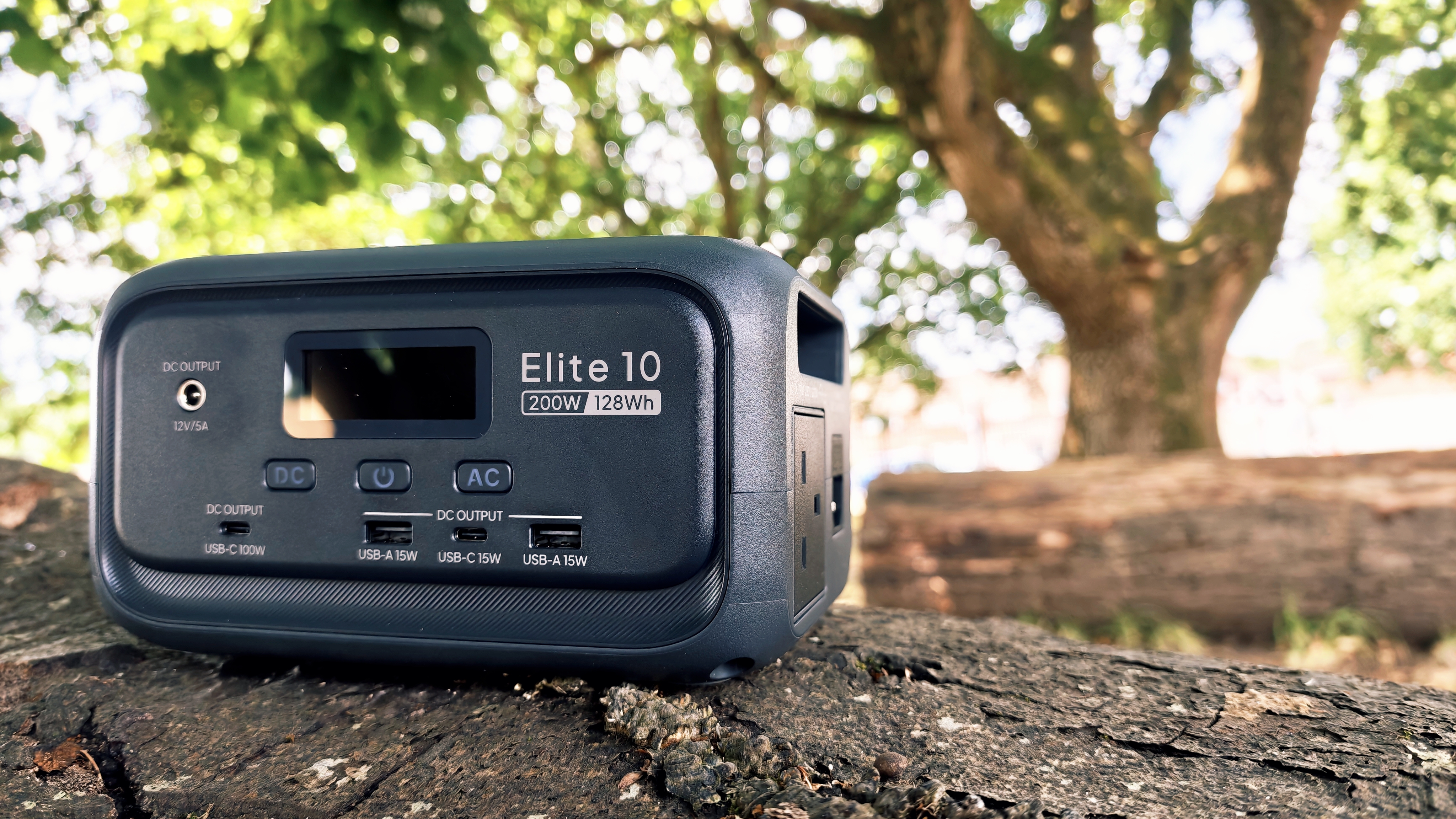 A grey Bluetti Elite 10 power station sitting on a log in a forest grove