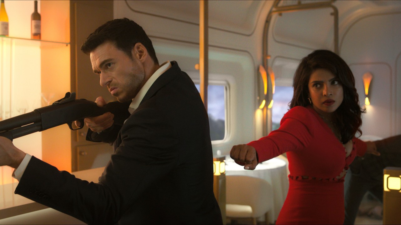 Richard Madden sosteniendo un arma y Priyanka Chopra detrás de él listos para pelear
