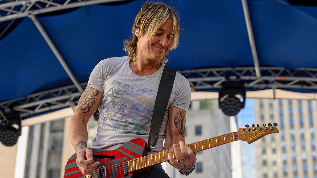 A close-up of Keith Urban smiling while playing guitar