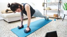 Woman in high plank position at home holding dumbbells