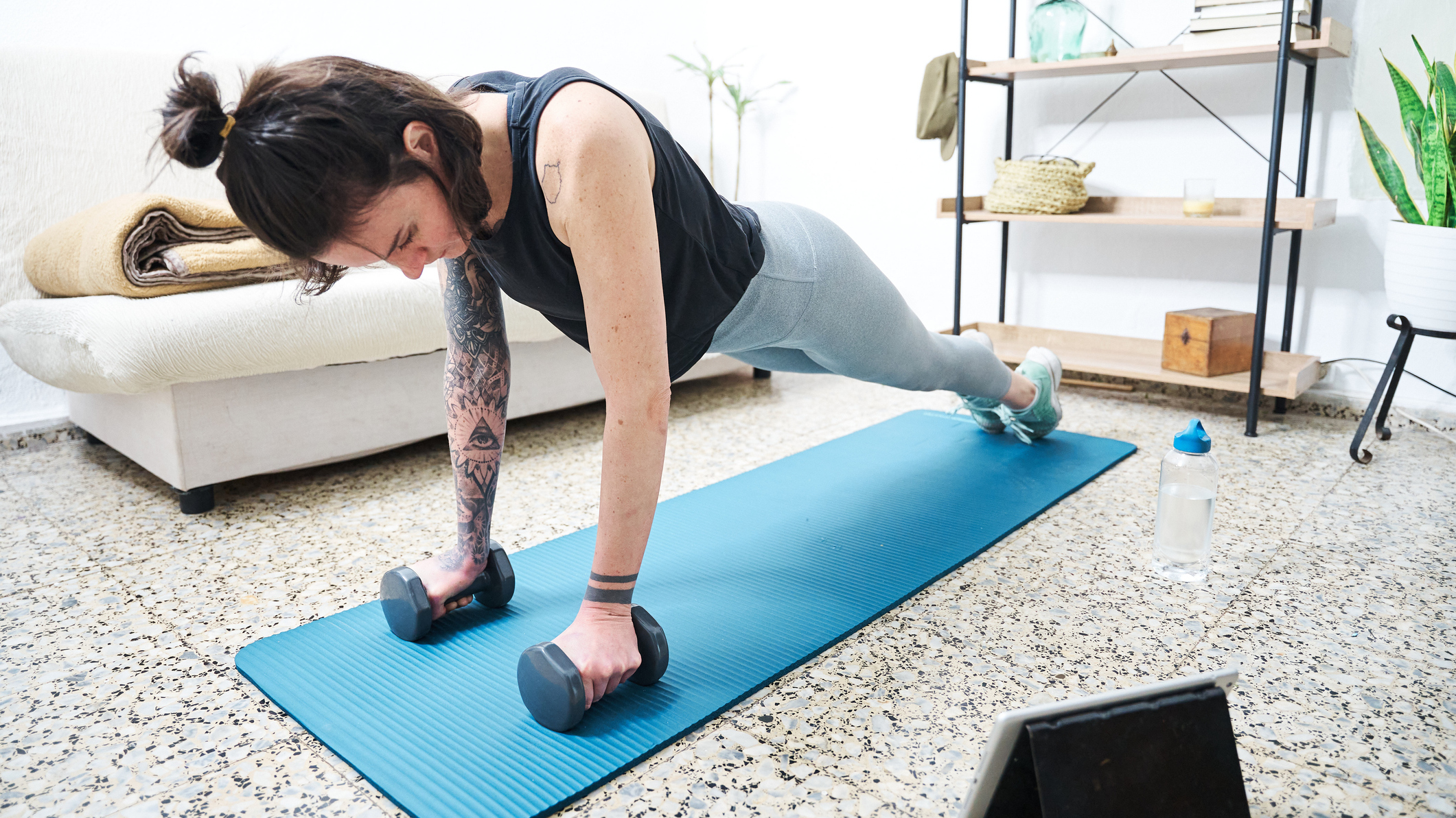 Woman in high plank position at home holding dumbbells