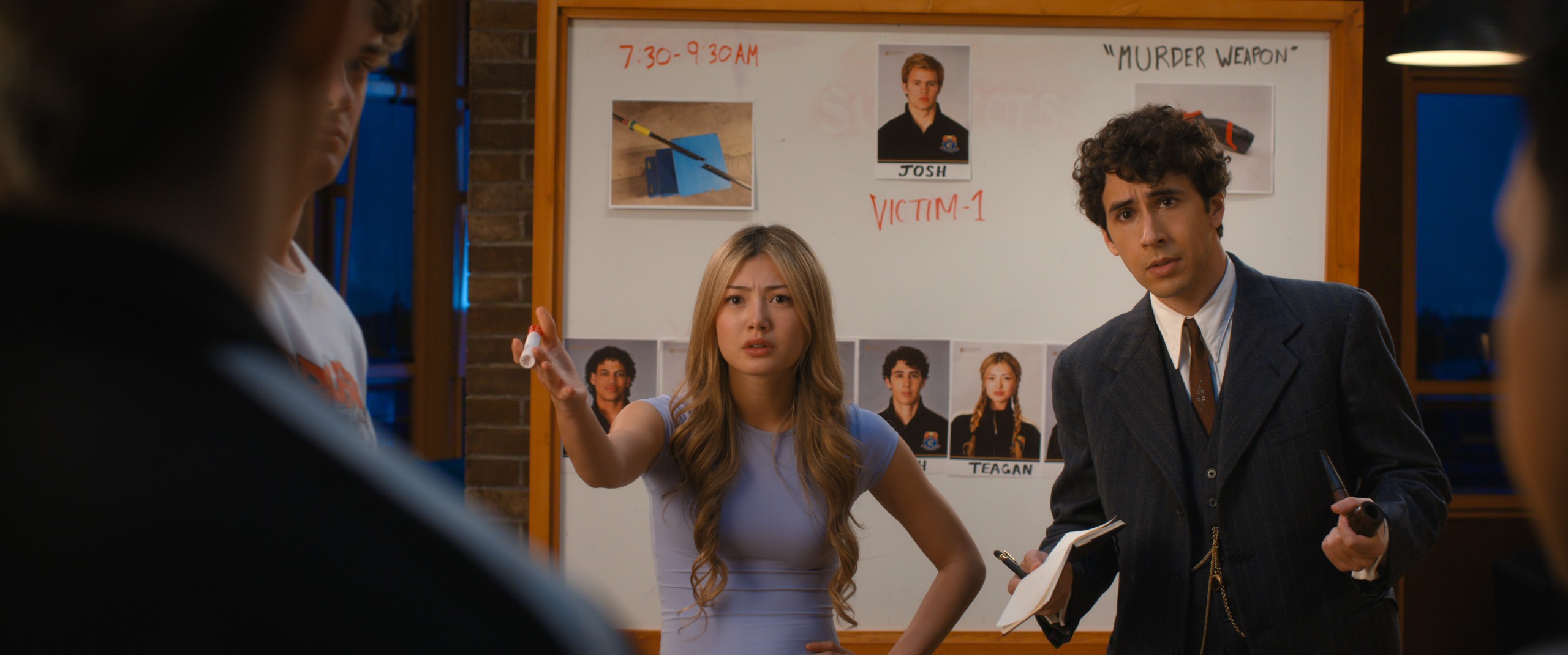 Two teenagers (Jude Wilson as Baloo Garner, Connor Wong as Perry Chou and Riley Davis as Noah Bainbridge) talk to a crowd while standing in front of a whiteboard, in Netflix's 'Crew Girl'.