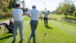 Golfer tees off watched by two playing partners