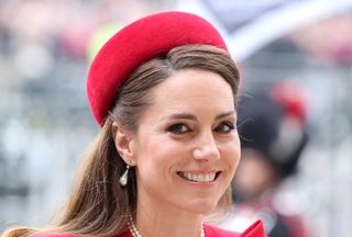 Kate Middleton wearing a red hat and pearl earrings smiling